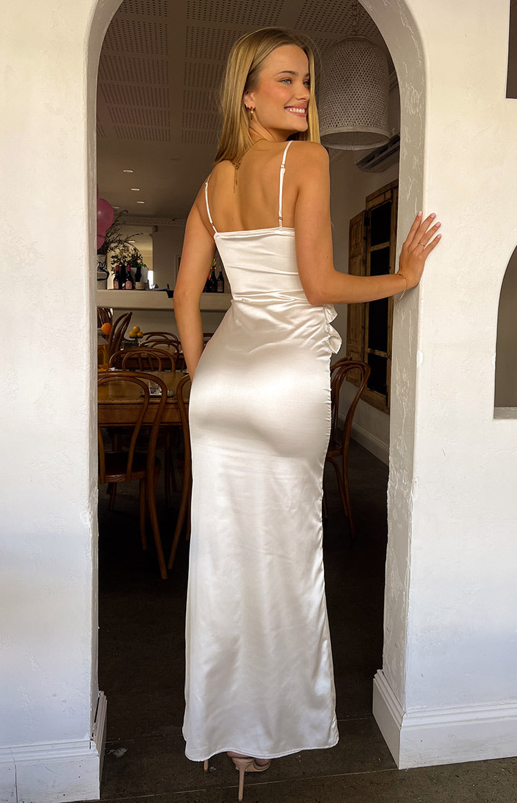 Girl wearing white satin maxi dress in front of restaurant tables.